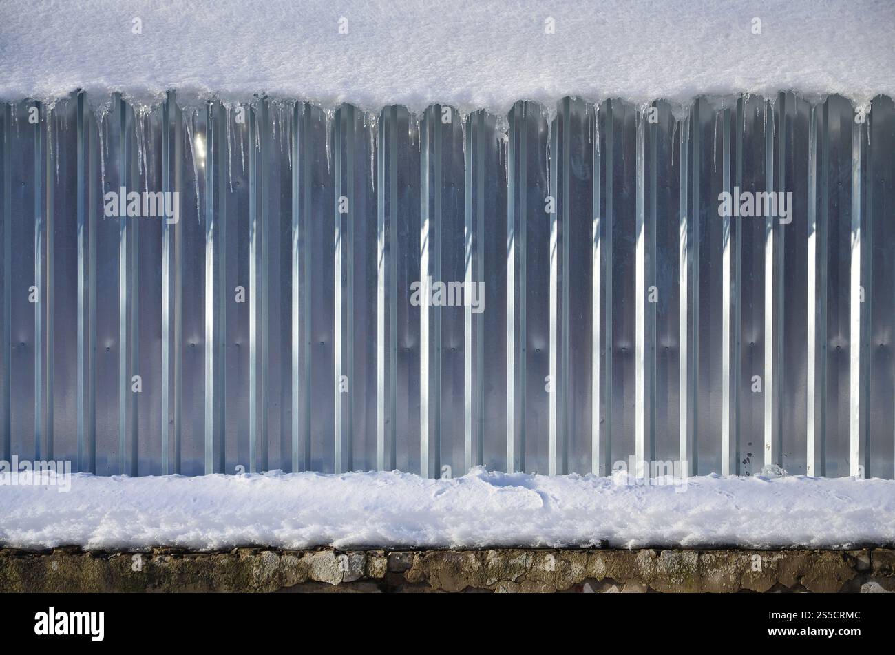 La texture del metallo lucido e delle pareti goffrate in pieno giorno in inverno con uno spesso strato di neve sopra. Struttura delle pareti in metallo innevato Foto Stock