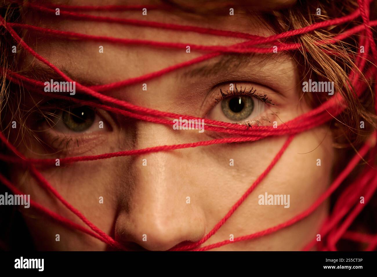 Primo piano di una parte del viso femminile con rughe chiare e grandi occhi verdi, la sua testa ricoperta di fili rossi Foto Stock