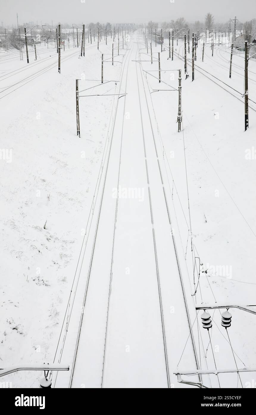 Paesaggio ferroviario invernale, binari ferroviari nel paese industriale innevato Foto Stock