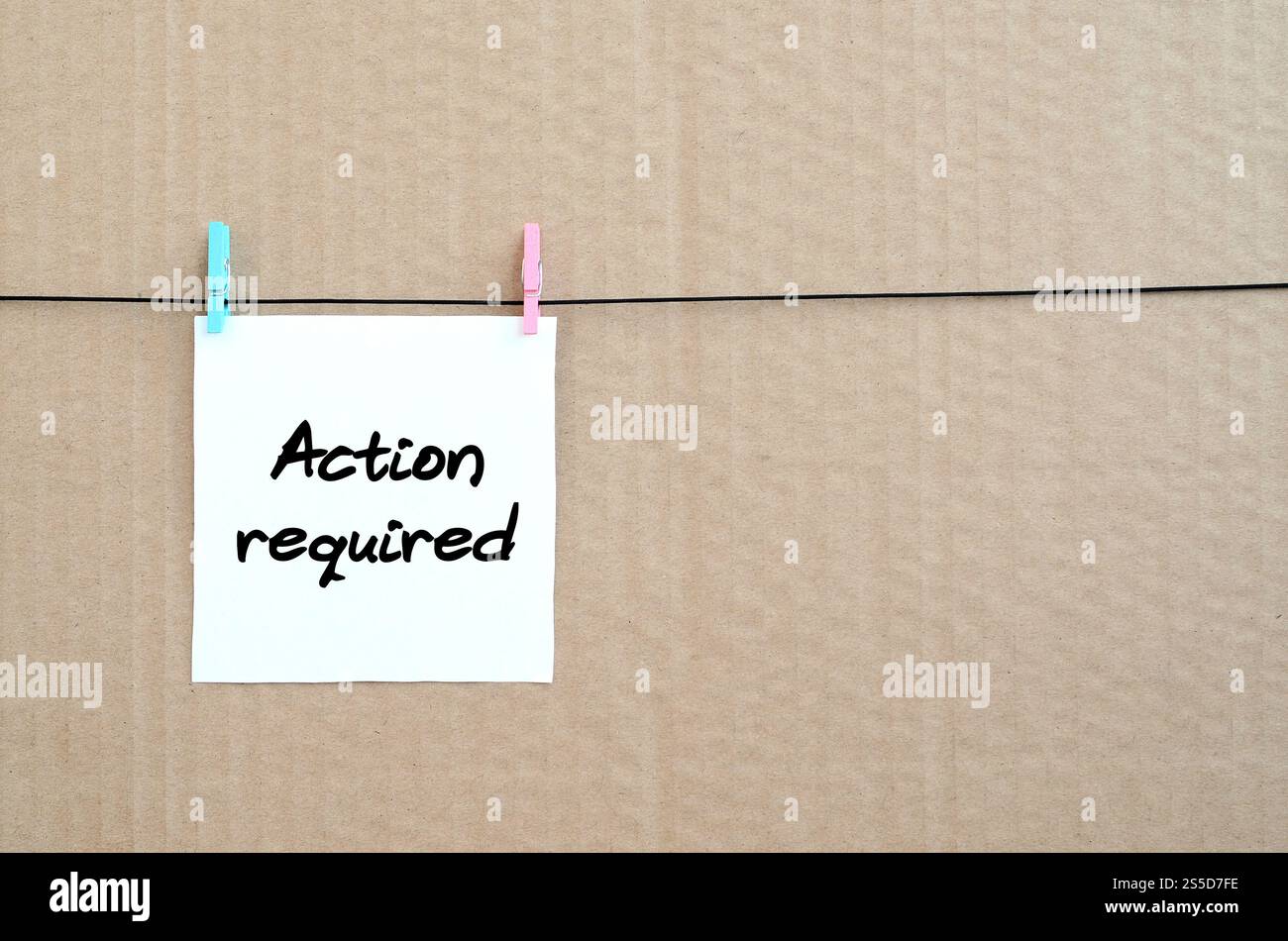 Azione richiesta! La nota è scritta su un adesivo bianco appeso a un clothespin su una corda su uno sfondo di cartone marrone Foto Stock