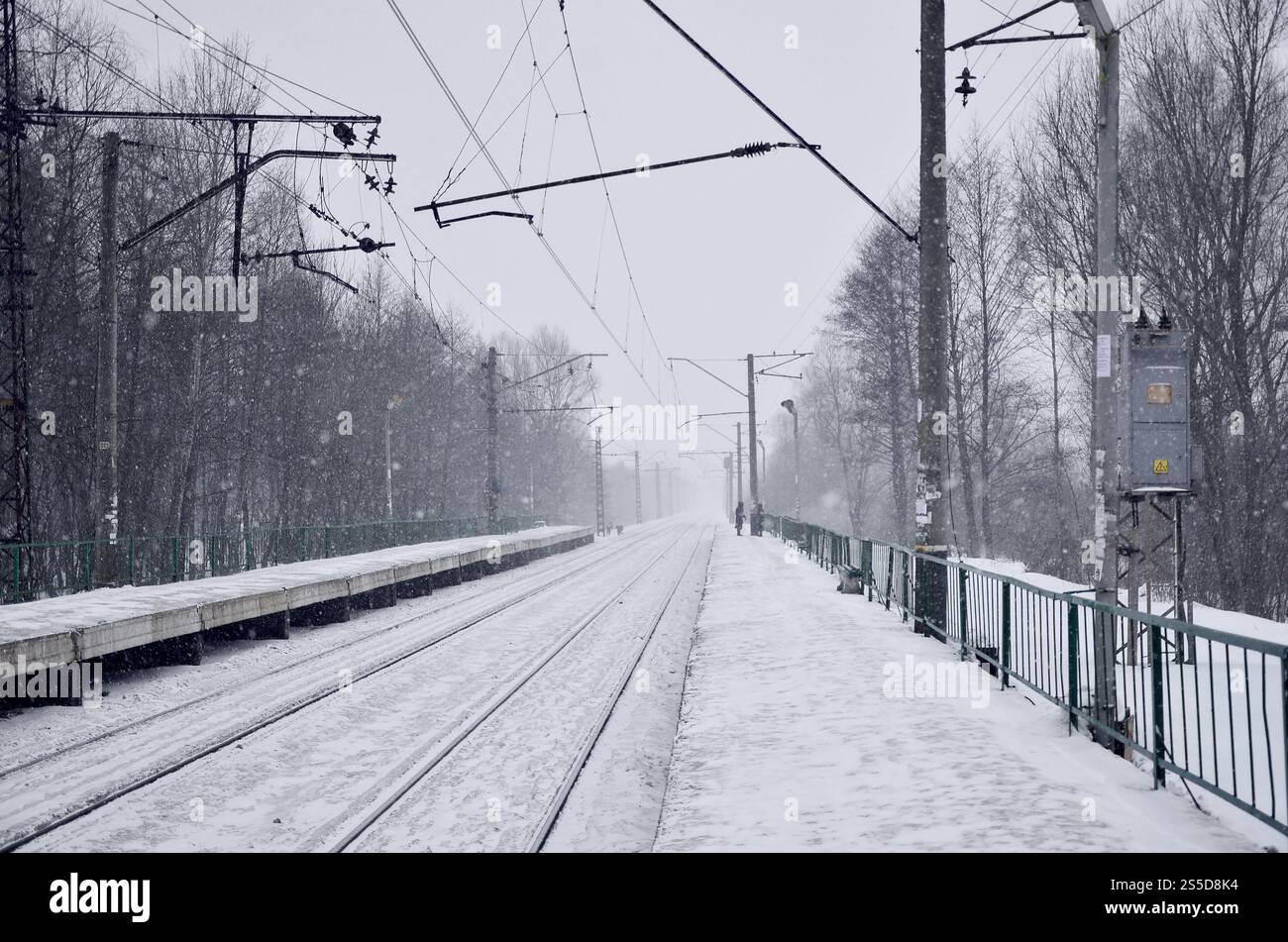 Stazione ferroviaria vuota in forte nevicata con fitta nebbia. Le rotaie si spengono in una nebbia bianca di neve. Il concetto di trasporto ferroviario in inverno. Foto Stock