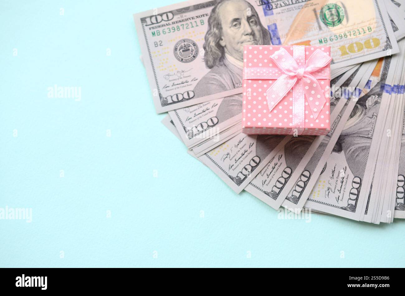 La confezione regalo rosa punteggiata si trova a circa cento banconote da un dollaro su sfondo azzurro. La confezione regalo rosa punteggiata si trova vicino a cento banconote da un dollaro su un blu chiaro Foto Stock