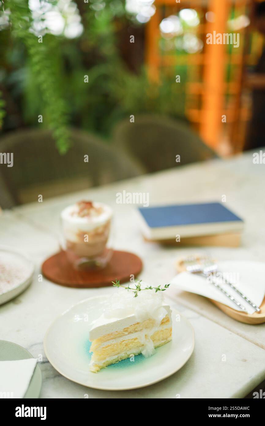 Torta al cocco e caffè in una caffetteria sullo sfondo sfocato. Dessert tradizionale a fette di deliziosa torta a strati di cocco. Foto Stock