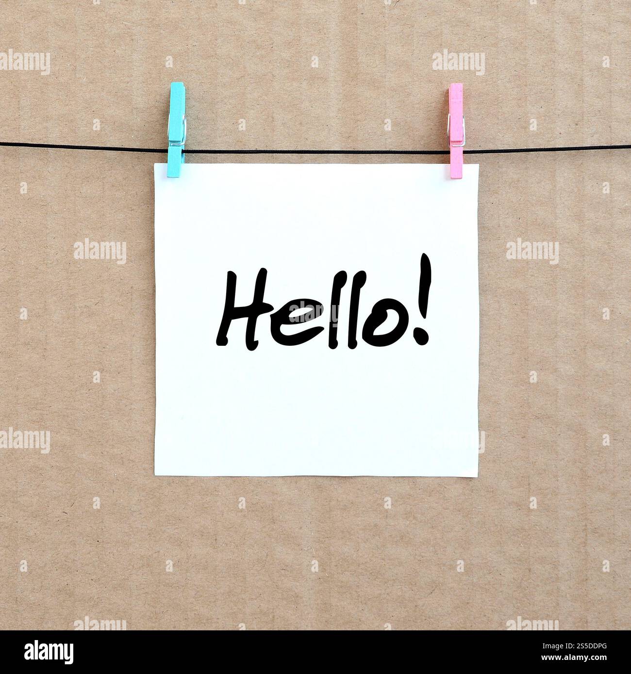Ciao! La nota è scritta su un adesivo bianco appeso a un clothespin su una corda su uno sfondo di cartone marrone Foto Stock