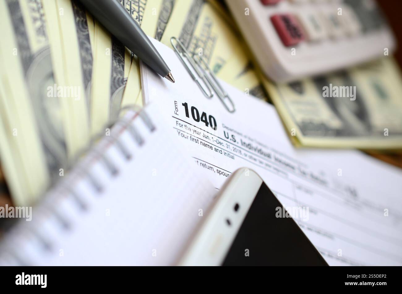 La penna, il notebook, la calcolatrice, lo smartphone e le fatture del dollaro si trova sul modulo di imposta 1040 US Reddito Individuale ritorno di imposta. Il tempo di pagare le tasse Foto Stock