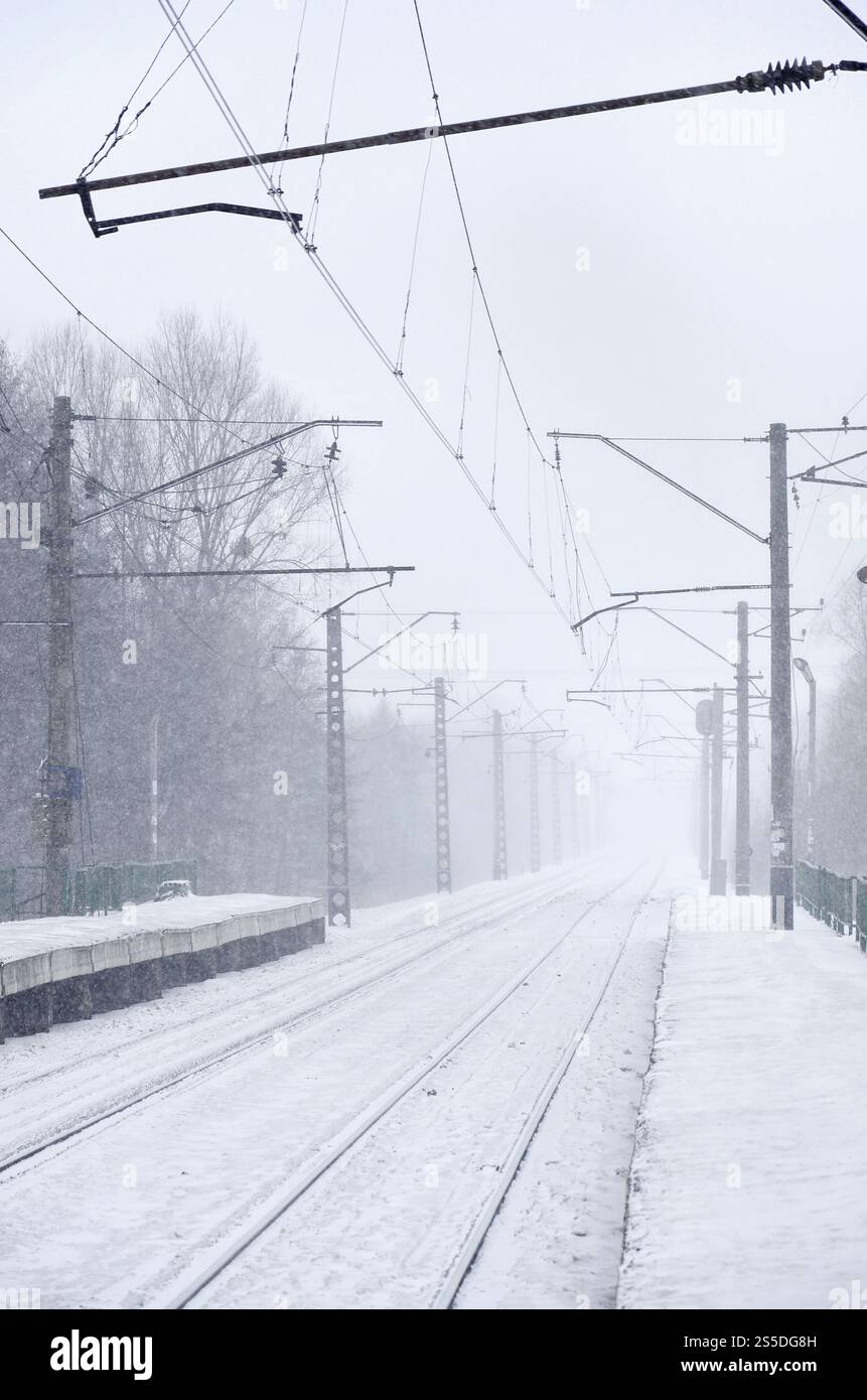Stazione ferroviaria vuota in forte nevicata con fitta nebbia. Le rotaie si spengono in una nebbia bianca di neve. Il concetto di trasporto ferroviario in inverno. Foto Stock