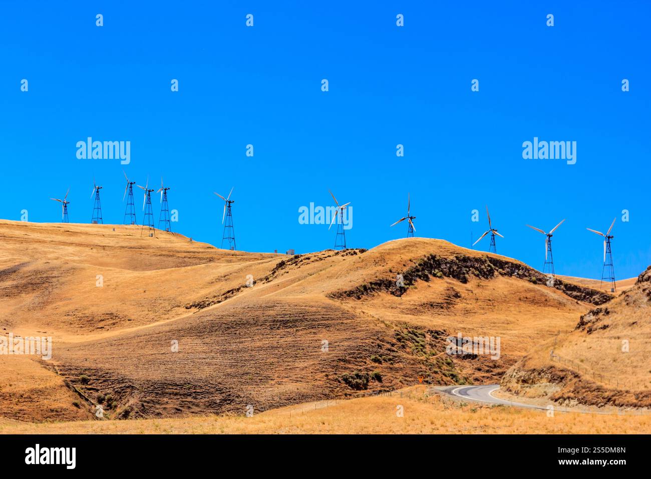 Una fila di mulini a vento si trova su una collina. I mulini a vento sono blu e sono distanziati. Il cielo è limpido e blu Foto Stock