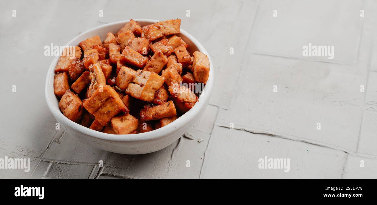 alcuni cubetti di tofu marinati, serviti come spuntino su una ciotola di ceramica bianca, su una superficie rustica in cemento, in formato panoramico da utilizzare come banner web Foto Stock
