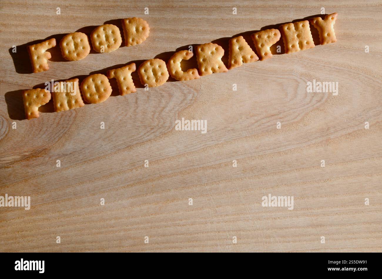 Fotografia gastronomica. Testo dai cracker salati come lettere inglesi stampate che giacciono su un tagliere di legno. Messaggio, fiancheggiato da lettere commestibili. Foto Stock