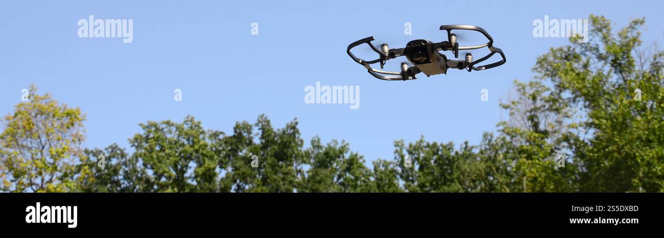 Drone con fotocamera decolla dalla terraferma e vola per scattare foto aeree al tramonto davanti agli alberi. Drone con fotocamera decollo da Foto Stock