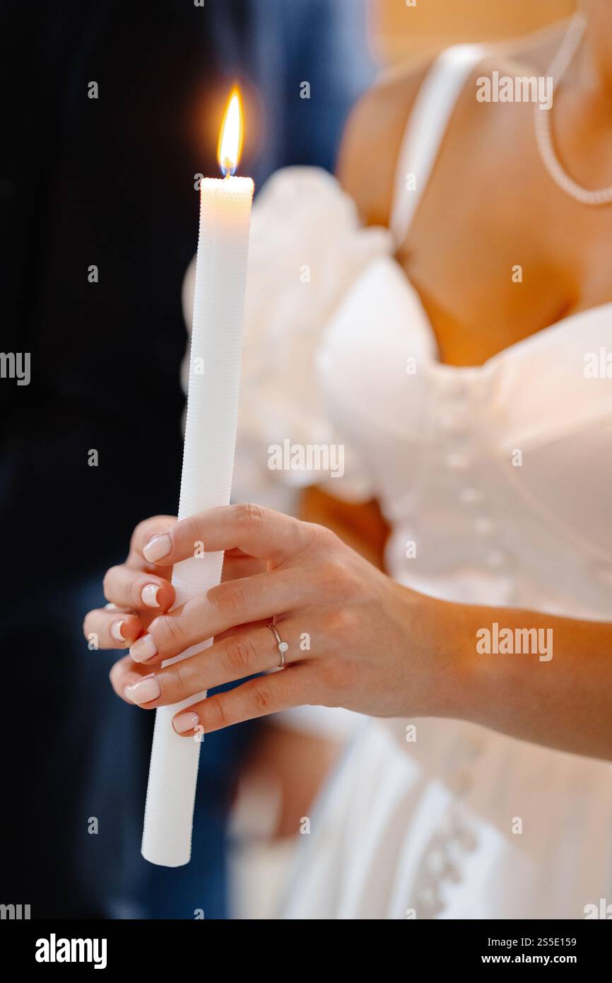 Primo piano delle mani della sposa che tengono una candela accesa durante una cerimonia nuziale, simboleggiando l'unità e la speranza Foto Stock