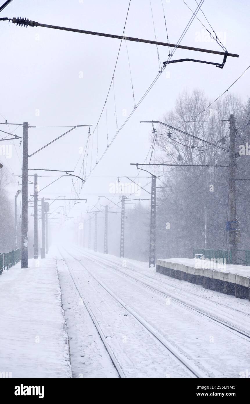 Stazione ferroviaria vuota in forte nevicata con fitta nebbia. Le rotaie si spengono in una nebbia bianca di neve. Il concetto di trasporto ferroviario in inverno. Foto Stock