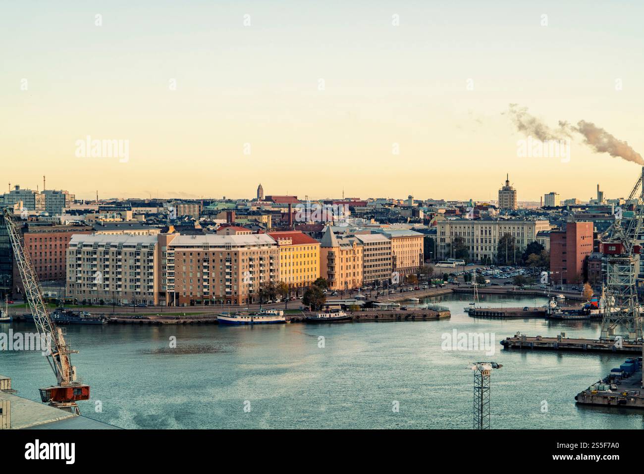 Vista aerea di una città al tramonto con edifici lungo il fiume e un'area industriale con cisterne, Helsinki, Finlandia Foto Stock