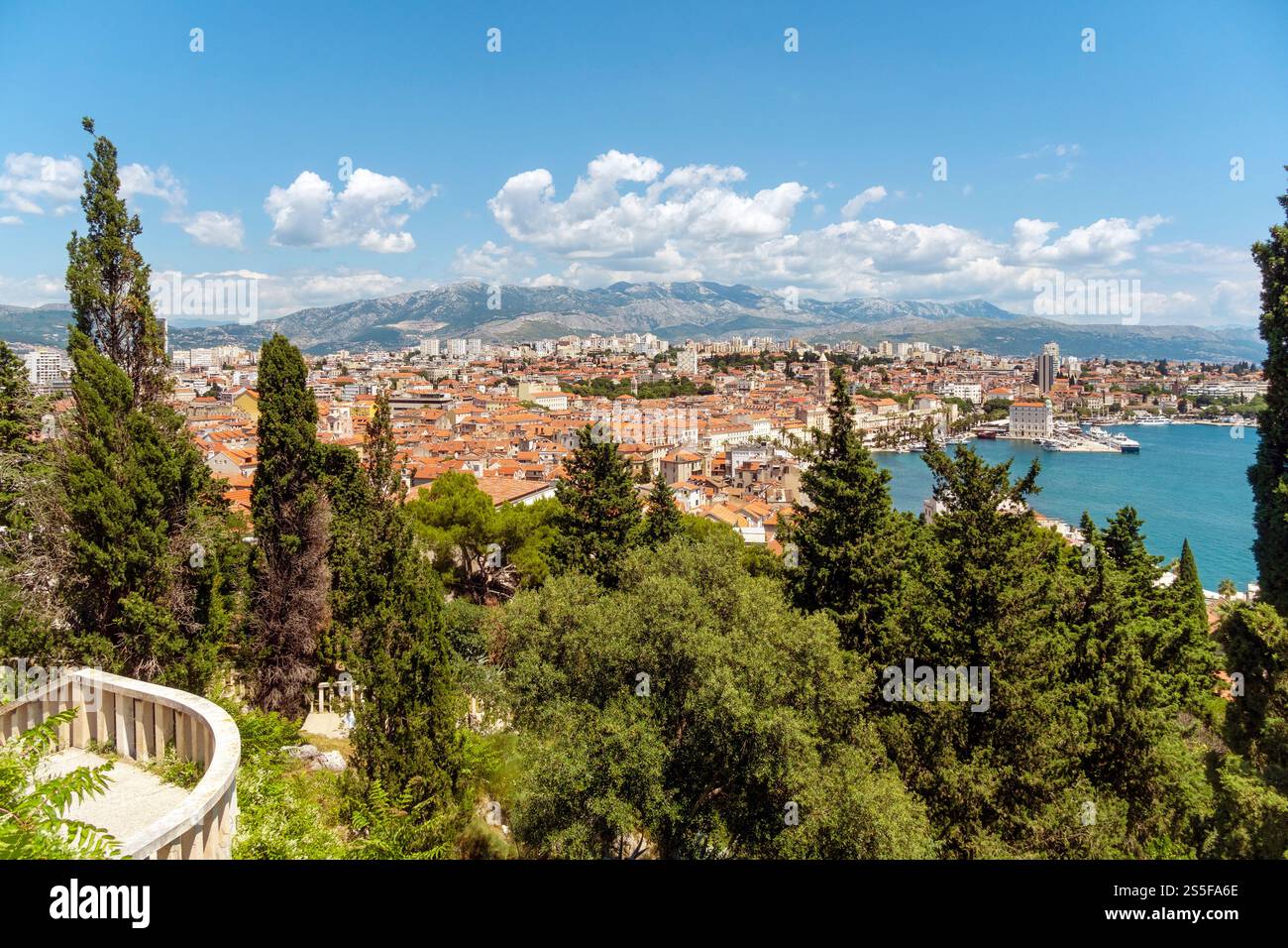 Vista sopraelevata di una città costiera di Spalato con tetti di tegole rosse, vegetazione lussureggiante e montagne sullo sfondo sotto un cielo azzurro e limpido, la Croazia Foto Stock