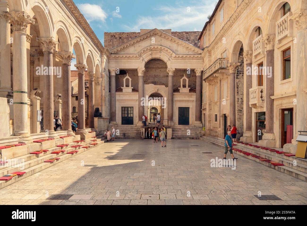 I turisti si riuniscono in una piazza storica con il Palazzo di Diocleziano, esplorando e scattando foto in una giornata di sole, Spalato, Croazia Foto Stock