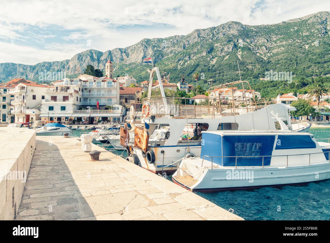 Città costiera di Drvenik con barca ormeggiata e sfondo di montagna sotto un cielo limpido, Drvenik, Croazia. Foto Stock