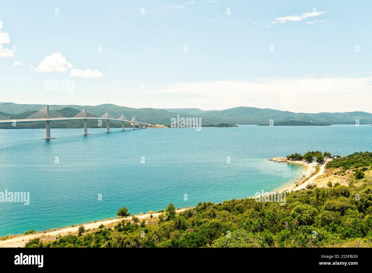 Paesaggio costiero caratterizzato da un lungo ponte sospeso Peljesac che si estende attraverso una baia blu con una lussureggiante costa verde sotto un cielo limpido, Peljesac, Croazia Foto Stock