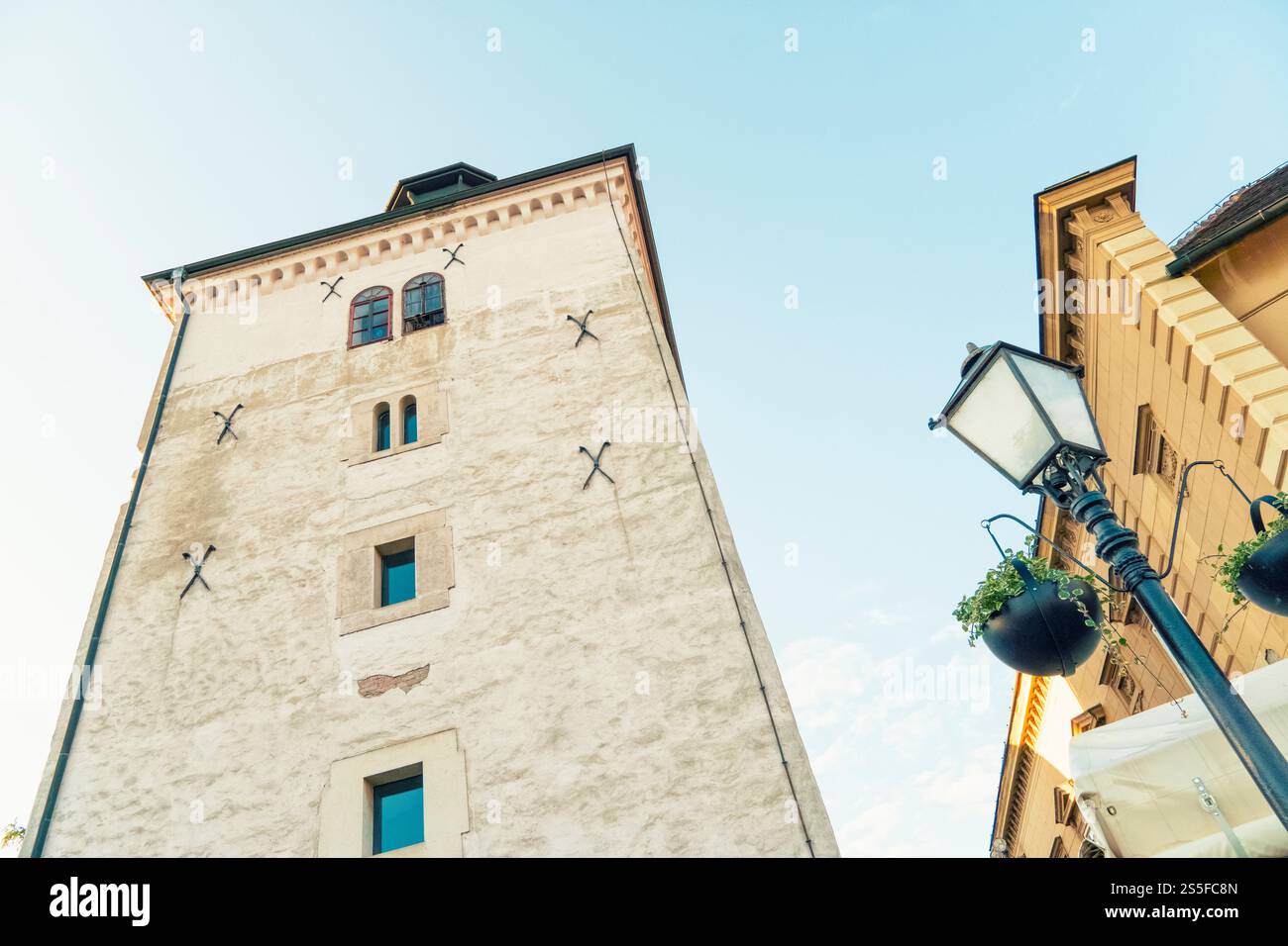 Torre bianca medievale con tetto verde sotto un cielo azzurro, fiancheggiata da edifici storici e lampioni adornati da piante appese, Zagabria, Croazia Foto Stock