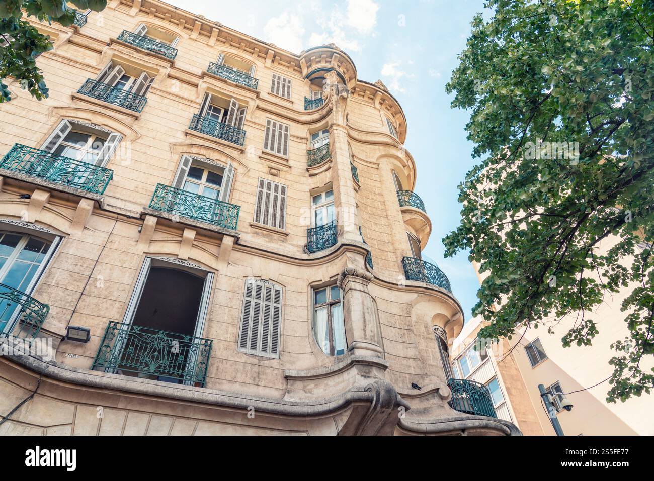 Elegante edificio parigino o provenzale con balconi in ferro battuto sotto un cielo azzurro, fiancheggiato da alberi verdi, Marsiglia, Francia Foto Stock