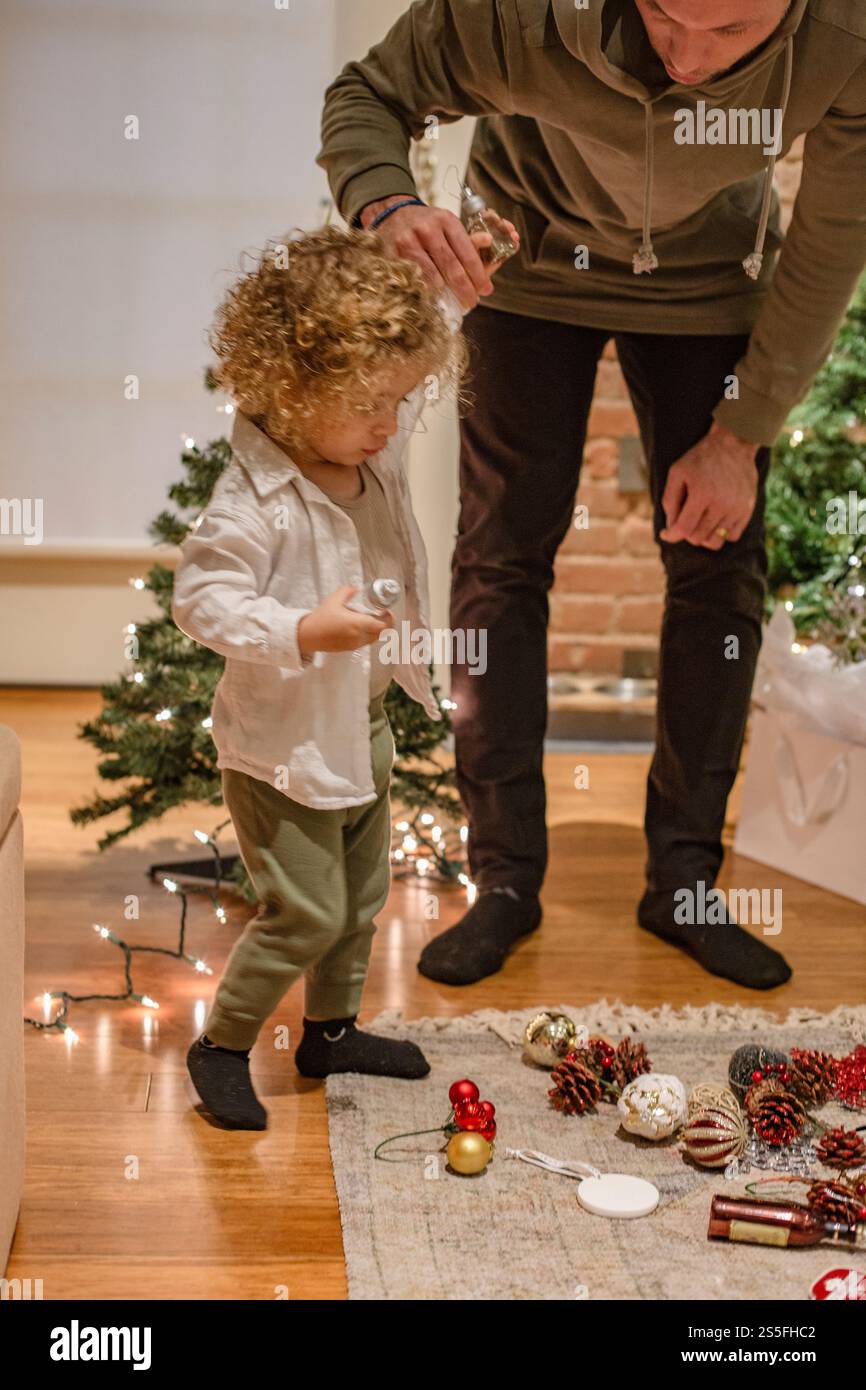 Adulto aiuta un bambino a decorare il Natale con luci scintillanti e ornamenti interni, Ohio, Stati Uniti Foto Stock