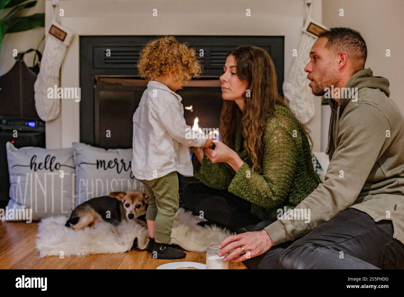 Una famiglia con un bambino piccolo e un cane seduti accanto al caminetto, un bambino turbato durante le festività, Ohio, Stati Uniti Foto Stock