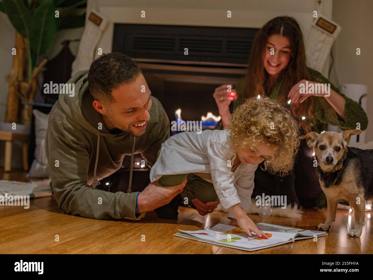 Famiglia che trascorre del tempo insieme al chiuso con un bambino che legge un libro e un cane che guarda, vicino al caminetto, Ohio, USA Foto Stock