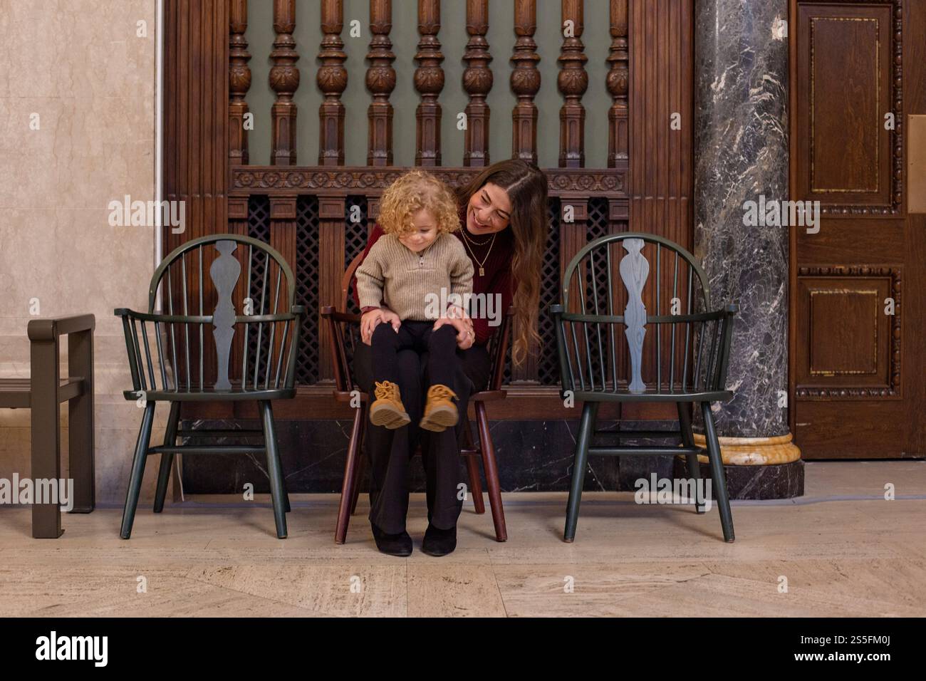 Donna sorridente seduta con un bambino su una panchina di legno in una biblioteca pubblica accanto a un grande pannello di legno, Cleveland Library, Ohio, USA Foto Stock