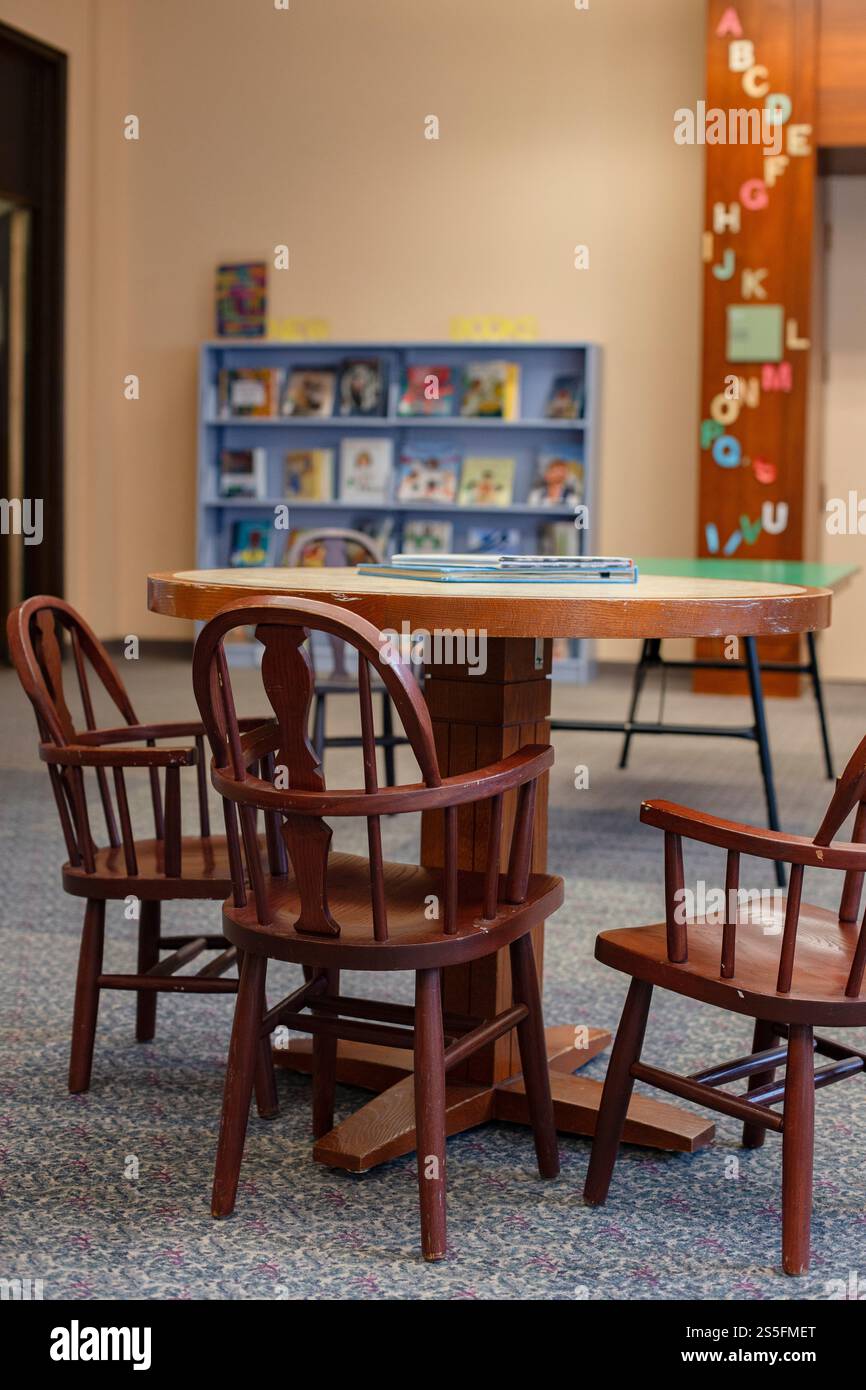 Sedie in legno che circondano un tavolo in una biblioteca con scaffali e arte da parete in alfabeto per bambini sullo sfondo. Cleveland, Ohio, Stati Uniti Foto Stock