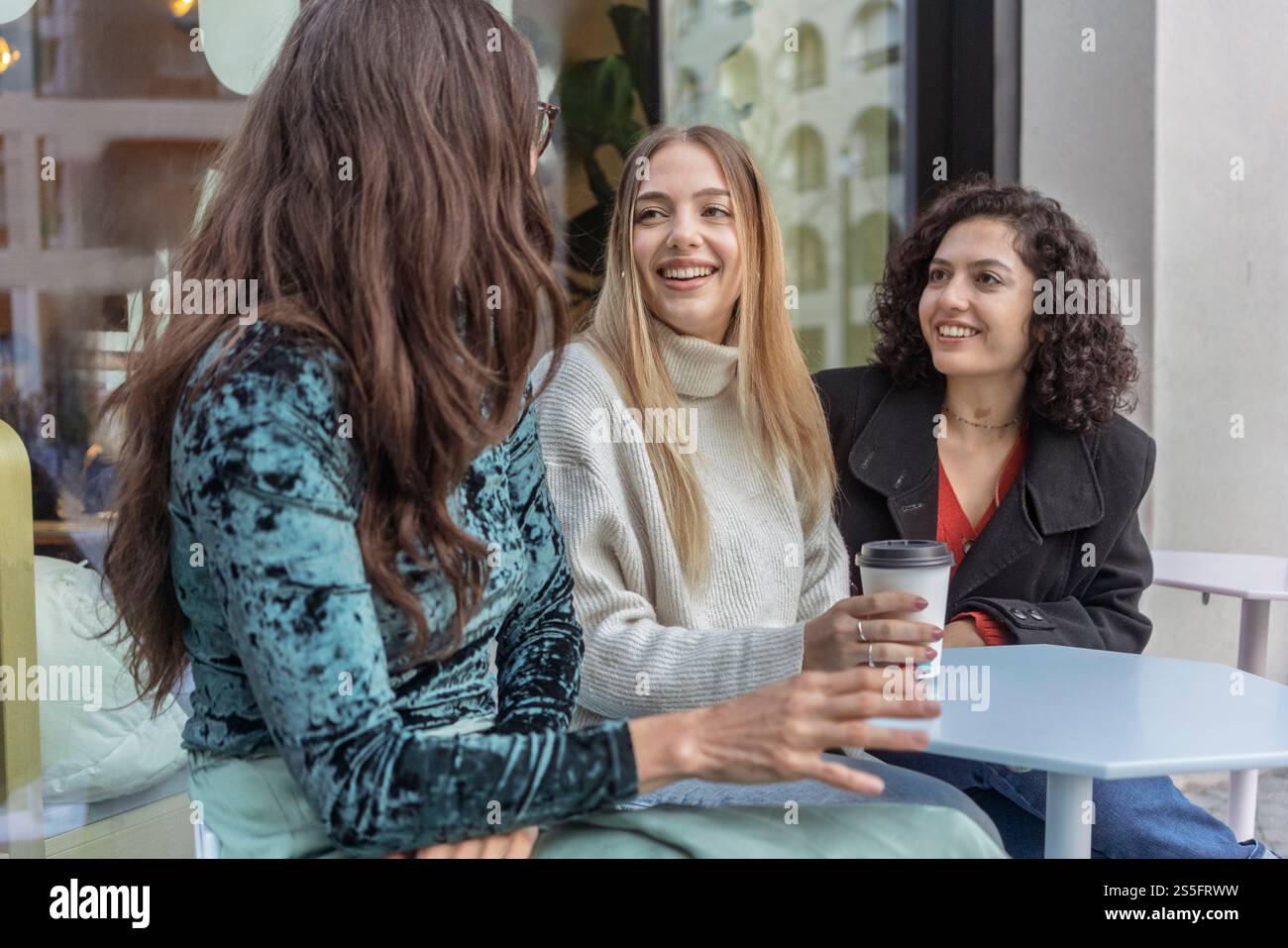 Tre donne stanno facendo una conversazione a un tavolo da caffè, una con una che tiene una tazza di caffè e sorride, Berlino, Germania Foto Stock