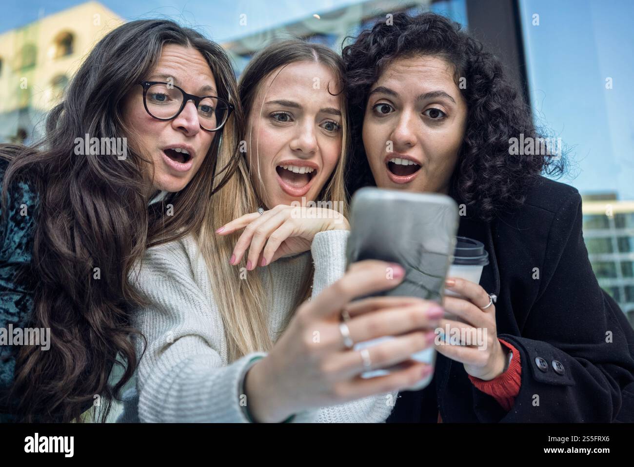 Tre donne entusiaste che scattano un selfie insieme a uno smartphone o vedono qualcosa di straordinario, Berlino, Germania Foto Stock