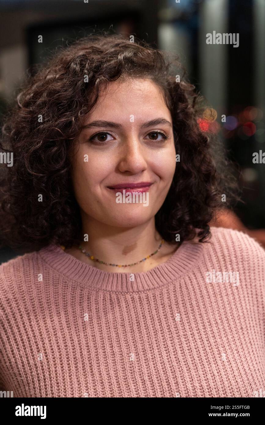 Donna sorridente con capelli marrone ricci che indossa un maglione rosa o un pullover al chiuso, Berlino, Germania Foto Stock
