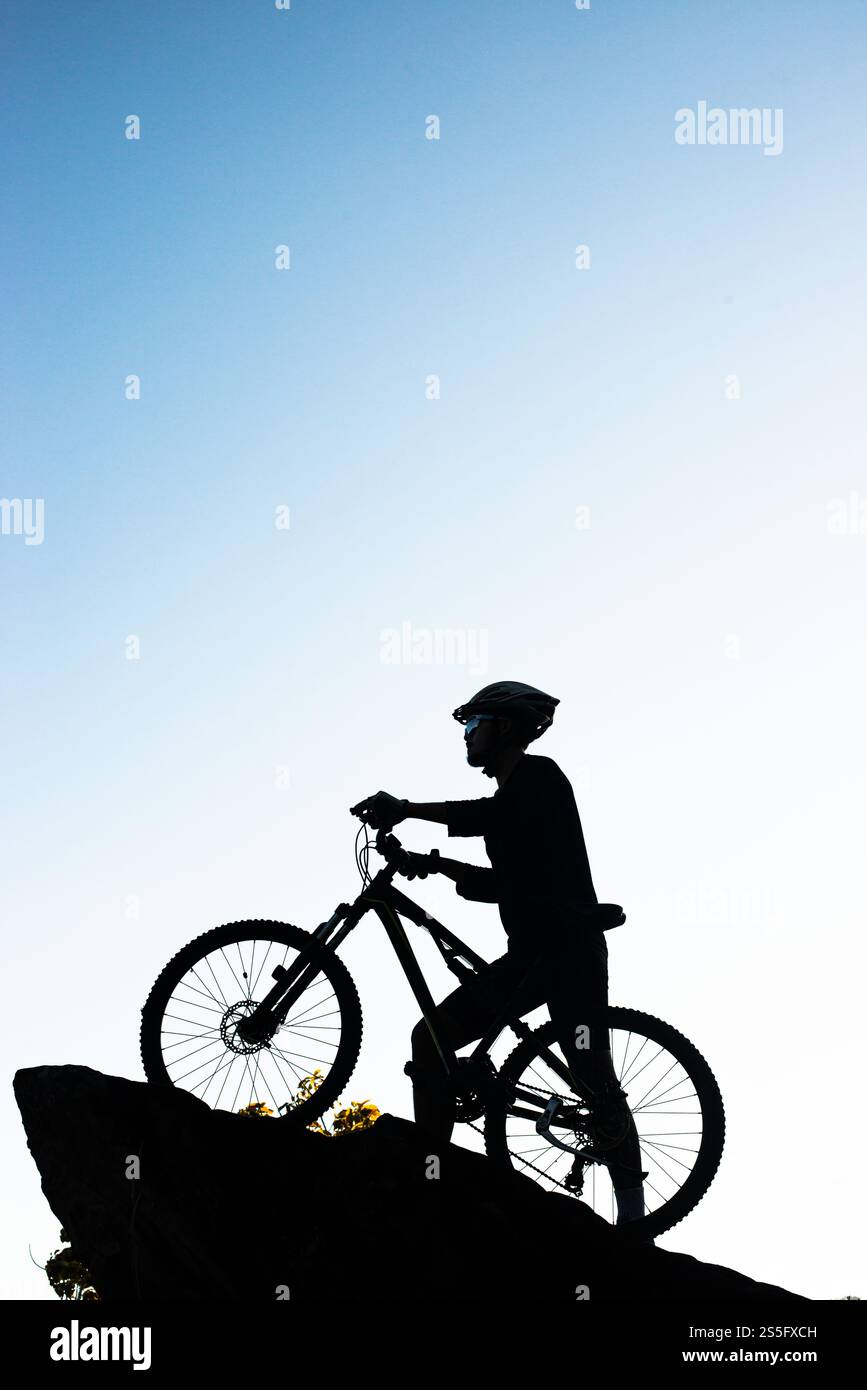 Silhouette dell'atleta in piedi sulla roccia con la bicicletta Foto Stock
