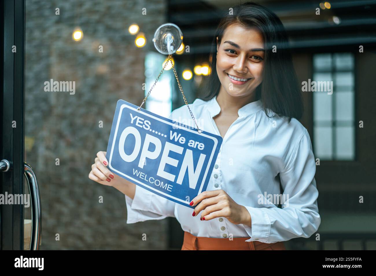 la donna sta in piedi e apre un ampio cartello attraverso la vetrina del negozio e sorride. Foto Stock