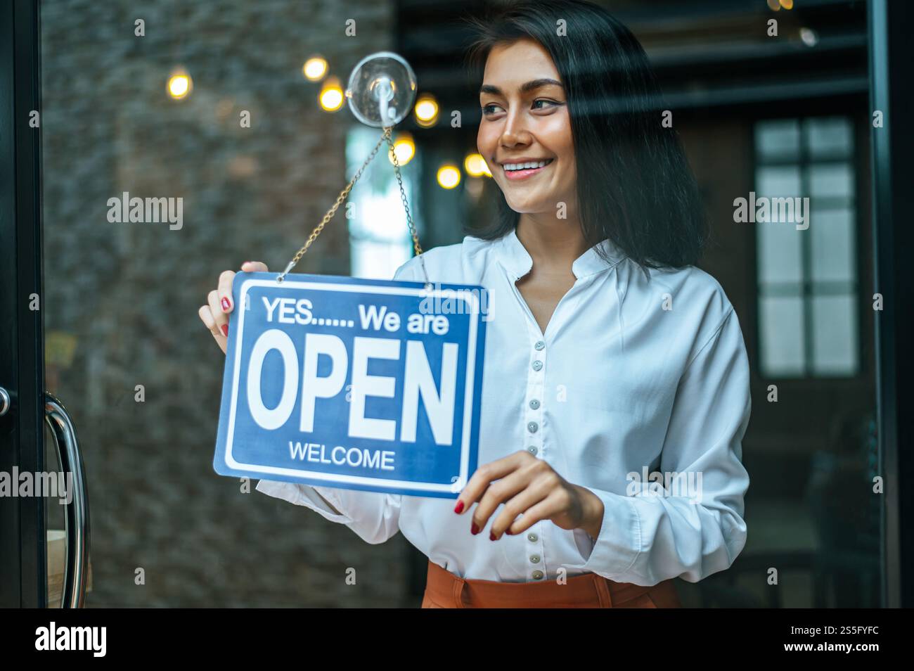 la donna sta in piedi e apre un ampio cartello attraverso la vetrina del negozio e sorride. Foto Stock