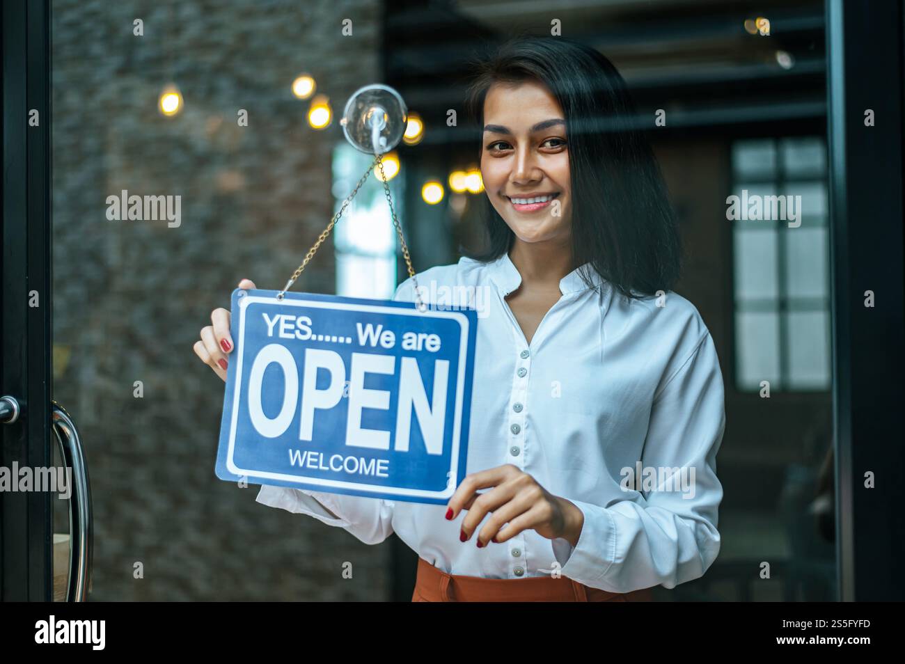 la donna sta in piedi e apre un ampio cartello attraverso la vetrina del negozio e sorride. Foto Stock