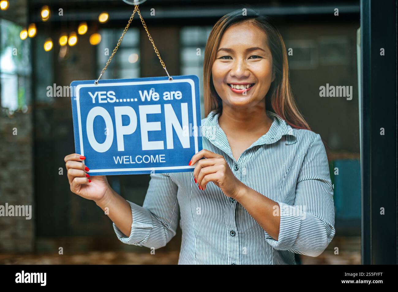 la donna sta in piedi e apre un ampio cartello attraverso la vetrina del negozio e sorride. Foto Stock