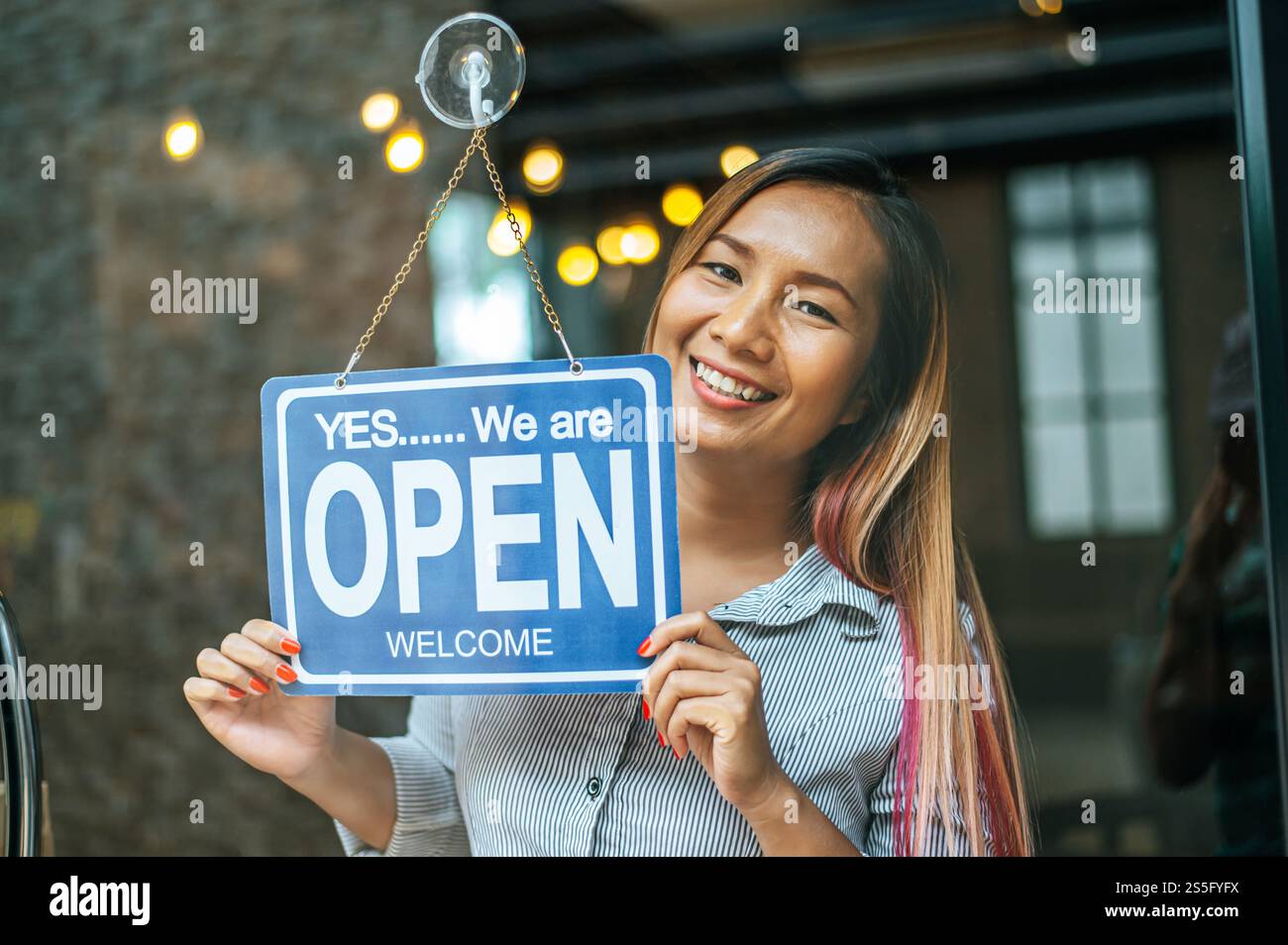 la donna sta in piedi e apre un ampio cartello attraverso la vetrina del negozio e sorride. Foto Stock
