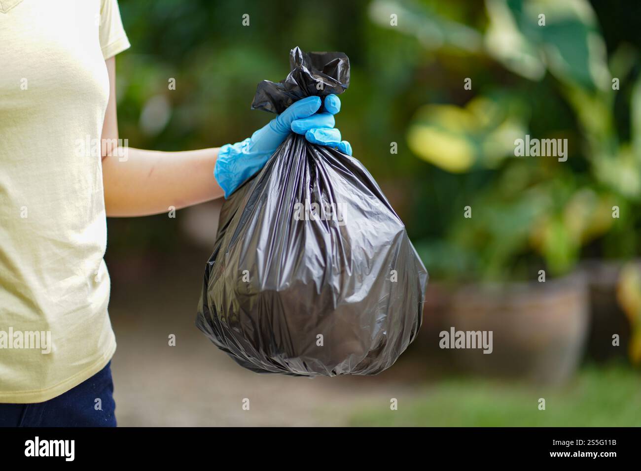 Donatrice volontaria che tiene a mano il sacchetto nero della spazzatura e la spazzatura della bottiglia di plastica per il riciclaggio per la pulizia nel parco volontariato concetto di riutilizzo e Foto Stock