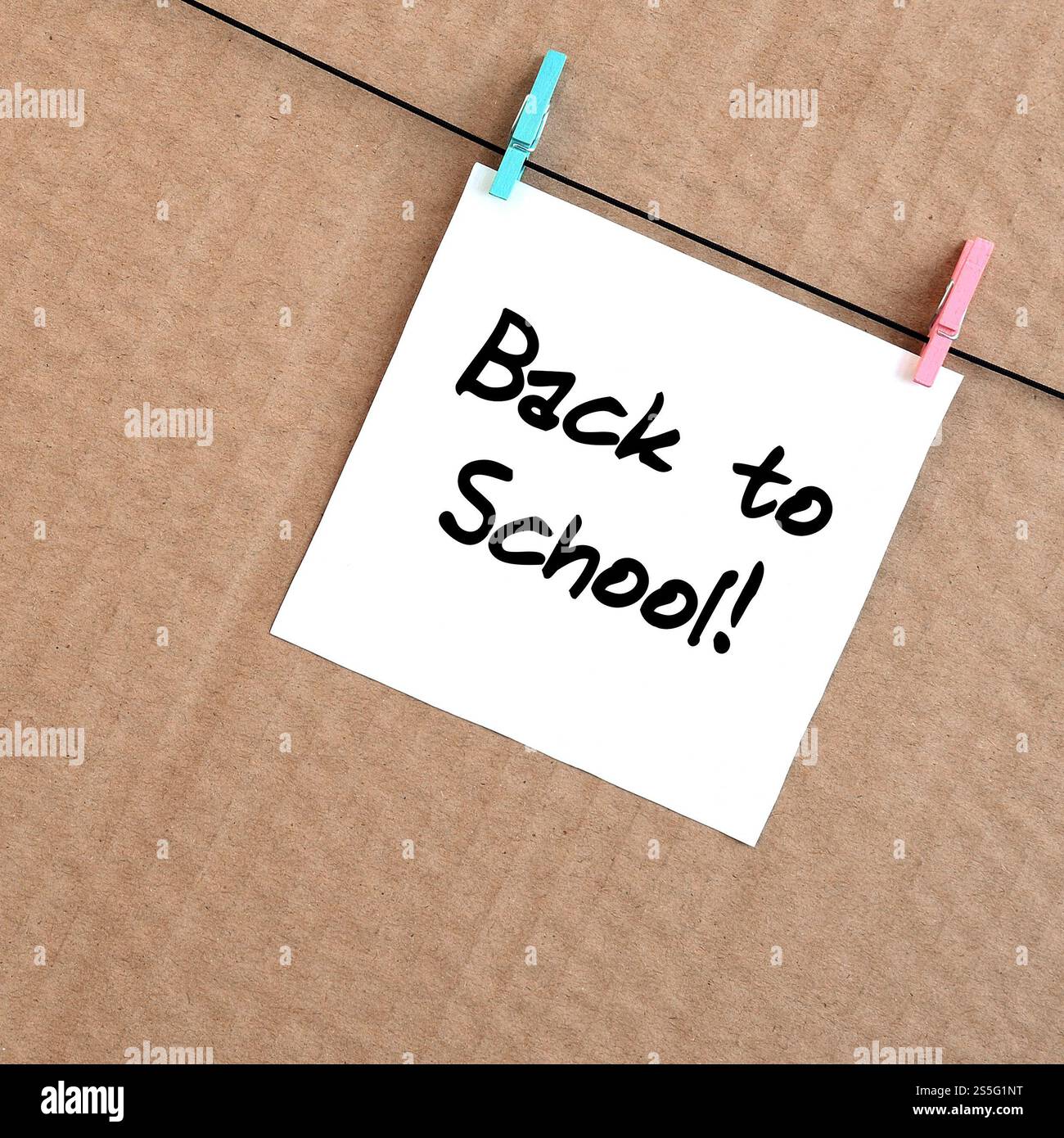 Torna a scuola! La nota è scritta su un adesivo bianco appeso a un clothespin su una corda su uno sfondo di cartone marrone Foto Stock