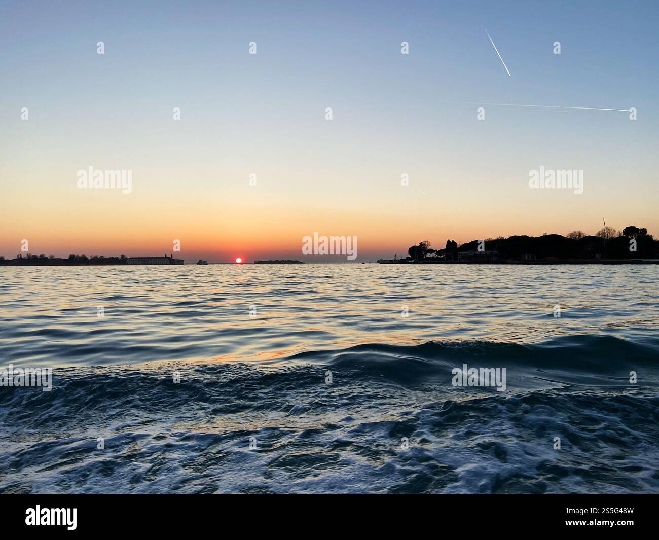 il sole si pone sotto la superficie dell'acqua all'orizzonte nella laguna veneta nella sera d'inverno Foto Stock