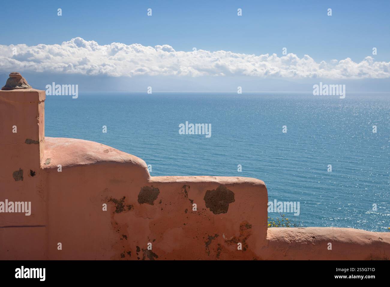 Vecchia recinzione strutturata dipinta di arancione. Vista sul Mar Tirreno, scintillante alla luce del sole. Cielo blu con nuvole bianche. Milazzo, Sicilia, Italia. Foto Stock