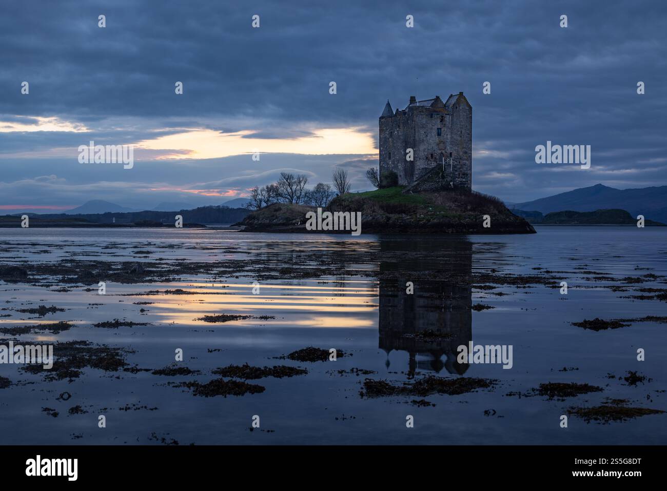 Lo storico castello di Castle Stalker si trova sul lago di Loch Laich, nelle Highlands scozzesi occidentali, mentre il sole tramonta sullo sfondo, Foto Stock
