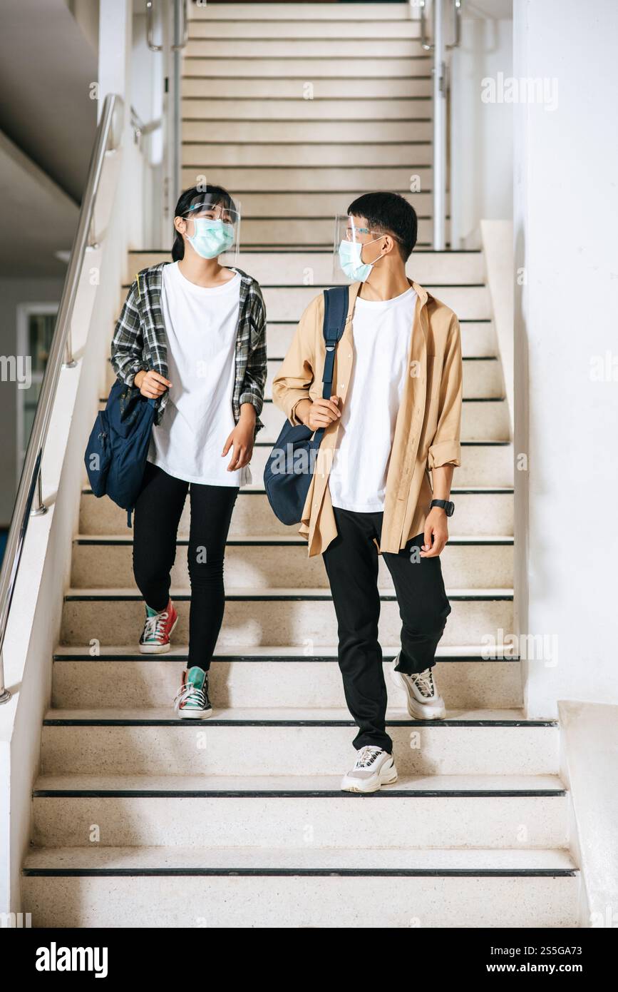 Gli studenti di sesso maschile e femminile indossano una maschera di salute e parlano tra loro sulle scale. Foto Stock