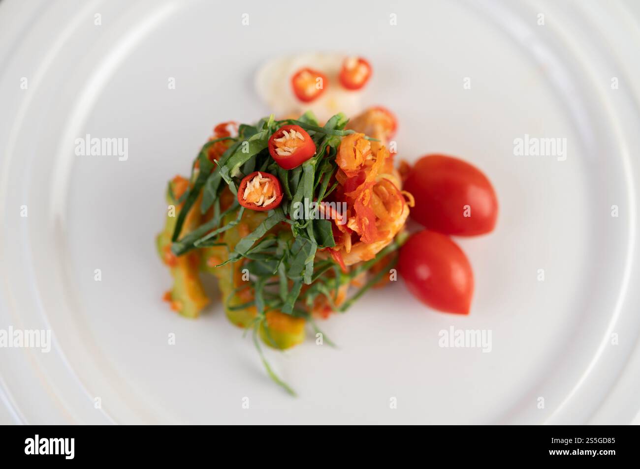 Peperoncini, foglie di calce kaffir, zucca amara e pomodori impilati su un piatto bianco. Messa a fuoco selettiva Foto Stock