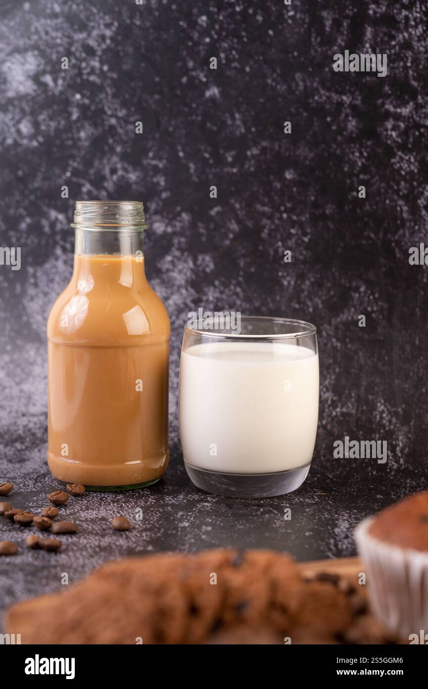 Caffè in una bottiglia con latte in un bicchiere su un pavimento di cemento nero. Messa a fuoco selettiva. Foto Stock