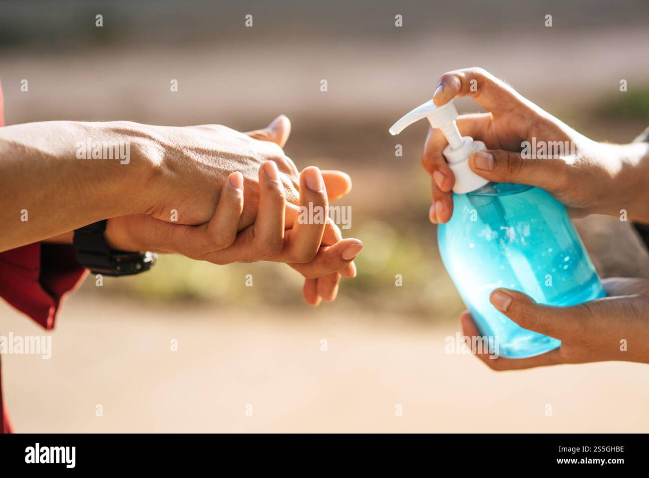 Mani in corrispondenza del flacone di gel per lavarsi le mani e stringere per consentire agli altri di lavarsi le mani. Foto Stock