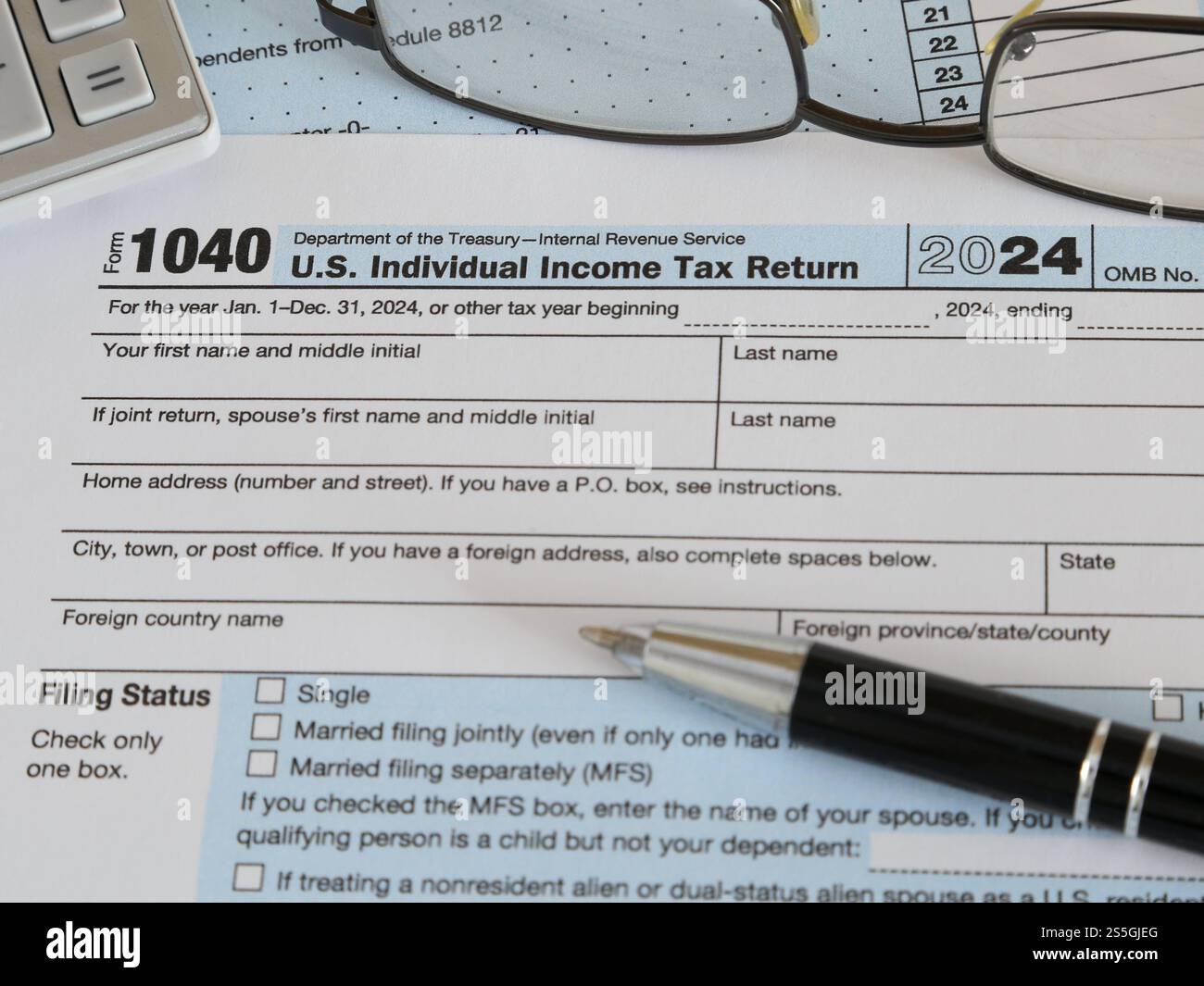 Nel 2025 viene mostrato un modulo IRS 1040 per l'anno fiscale 2024, insieme a una penna a inchiostro, una calcolatrice e degli occhiali. Foto Stock