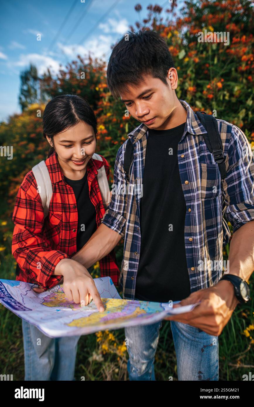 I turisti uomini e donne guardano la mappa vicino ai giardini fioriti. Foto Stock