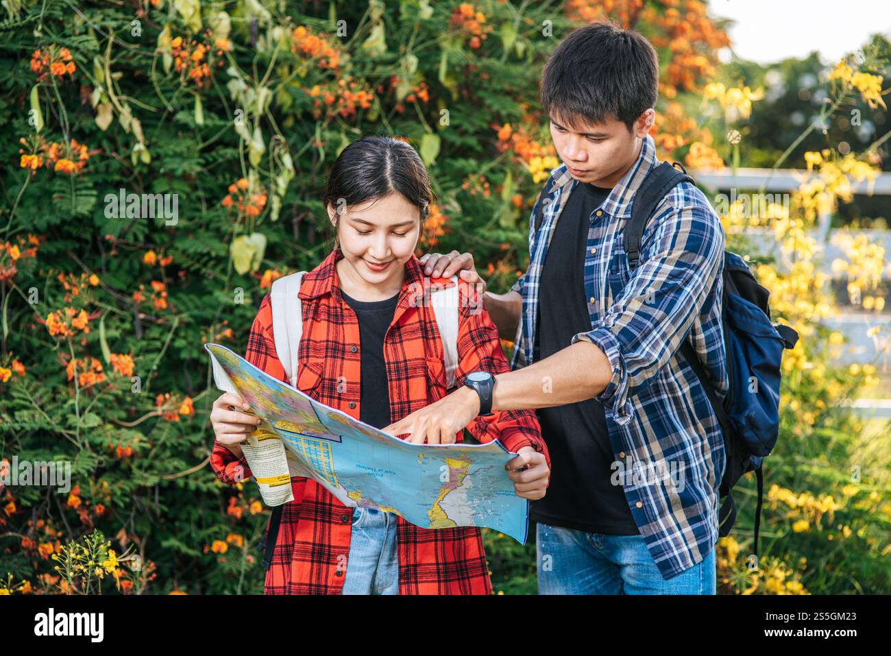 I turisti uomini e donne guardano la mappa vicino ai giardini fioriti. Foto Stock