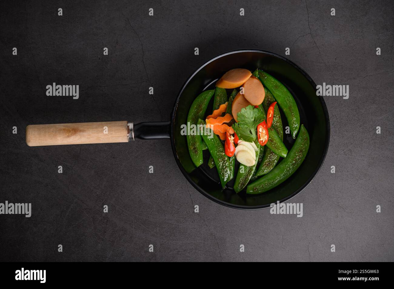 Mescolare i piselli fritti in una padella su fondo di cemento nero. Vista dall'alto. Foto Stock
